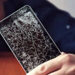 Person holding a smartphone with a severely cracked screen