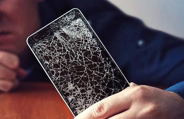 Person holding a smartphone with a severely cracked screen