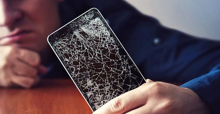 Person holding a smartphone with a severely cracked screen