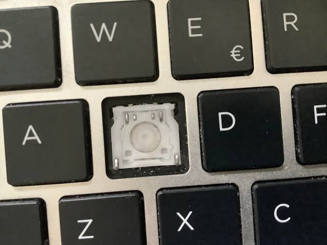 Close-up of a laptop keyboard with the S key removed, showing the switch mechanism underneath